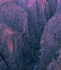 A deep canyon with nearly vertical sides, formed of dark rock with a magenta cast.